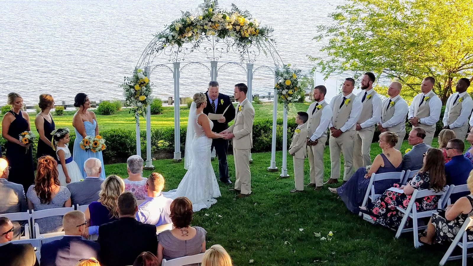 An outdoor waterfront ceremony under a flower-covered gazebo