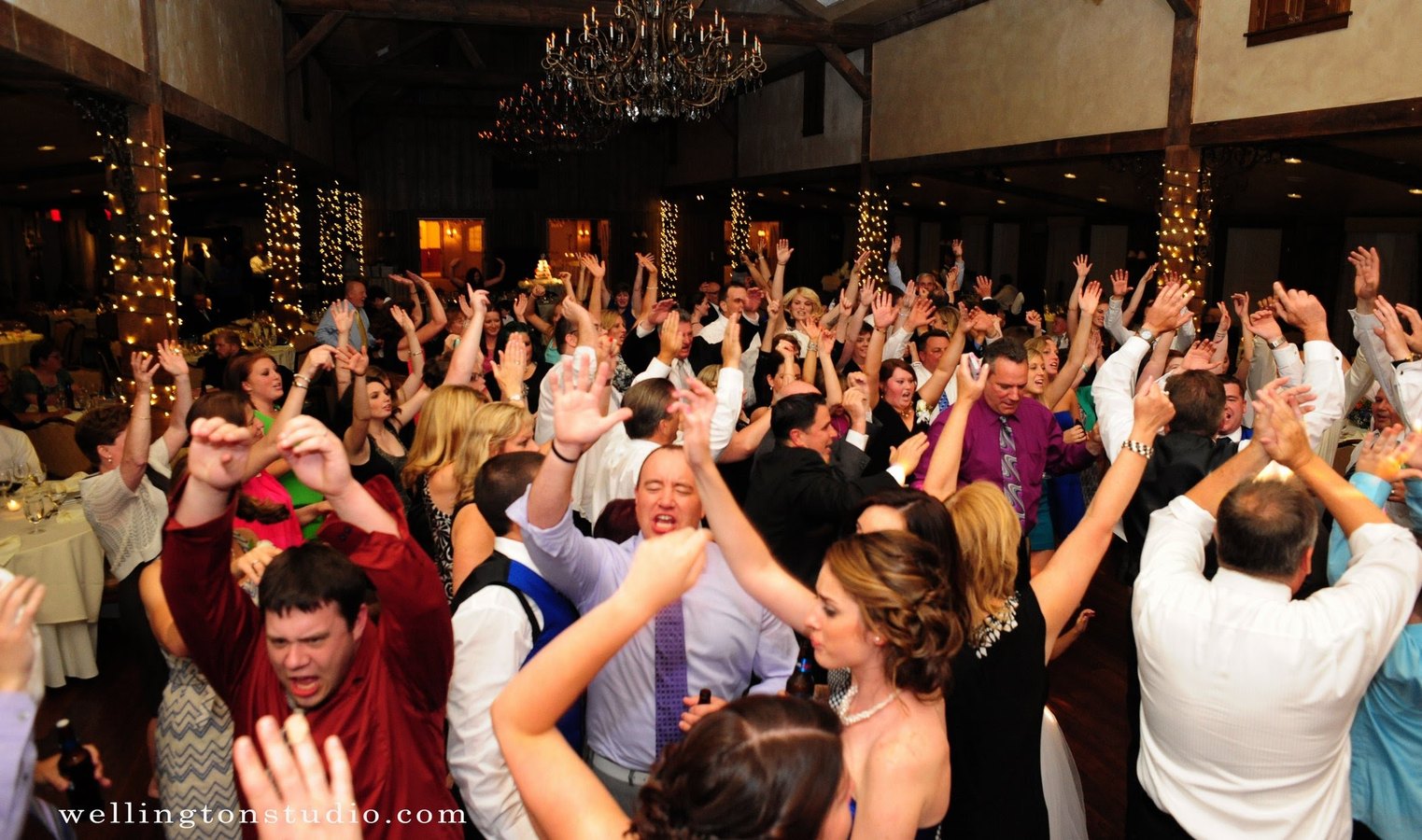 A full reception dance floor under a chandelier, arms raised