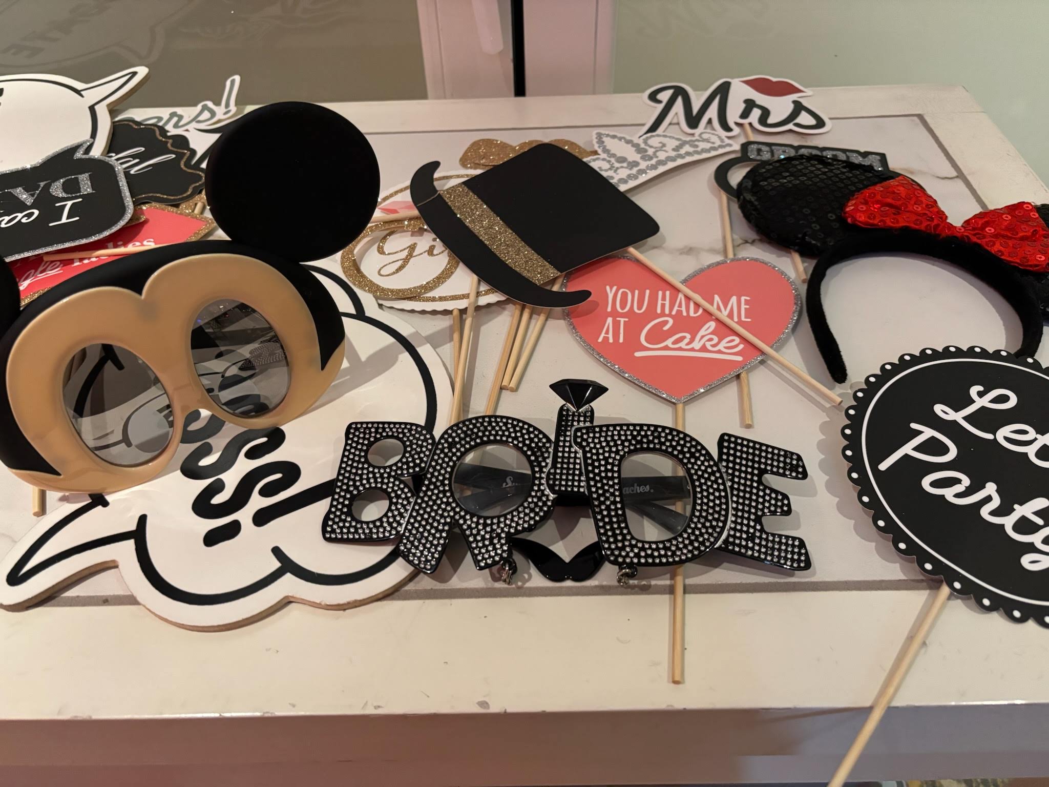 A table of photo booth props: BRIDE glasses, a Mrs sign, top hats and a “You Had Me At Cake” heart