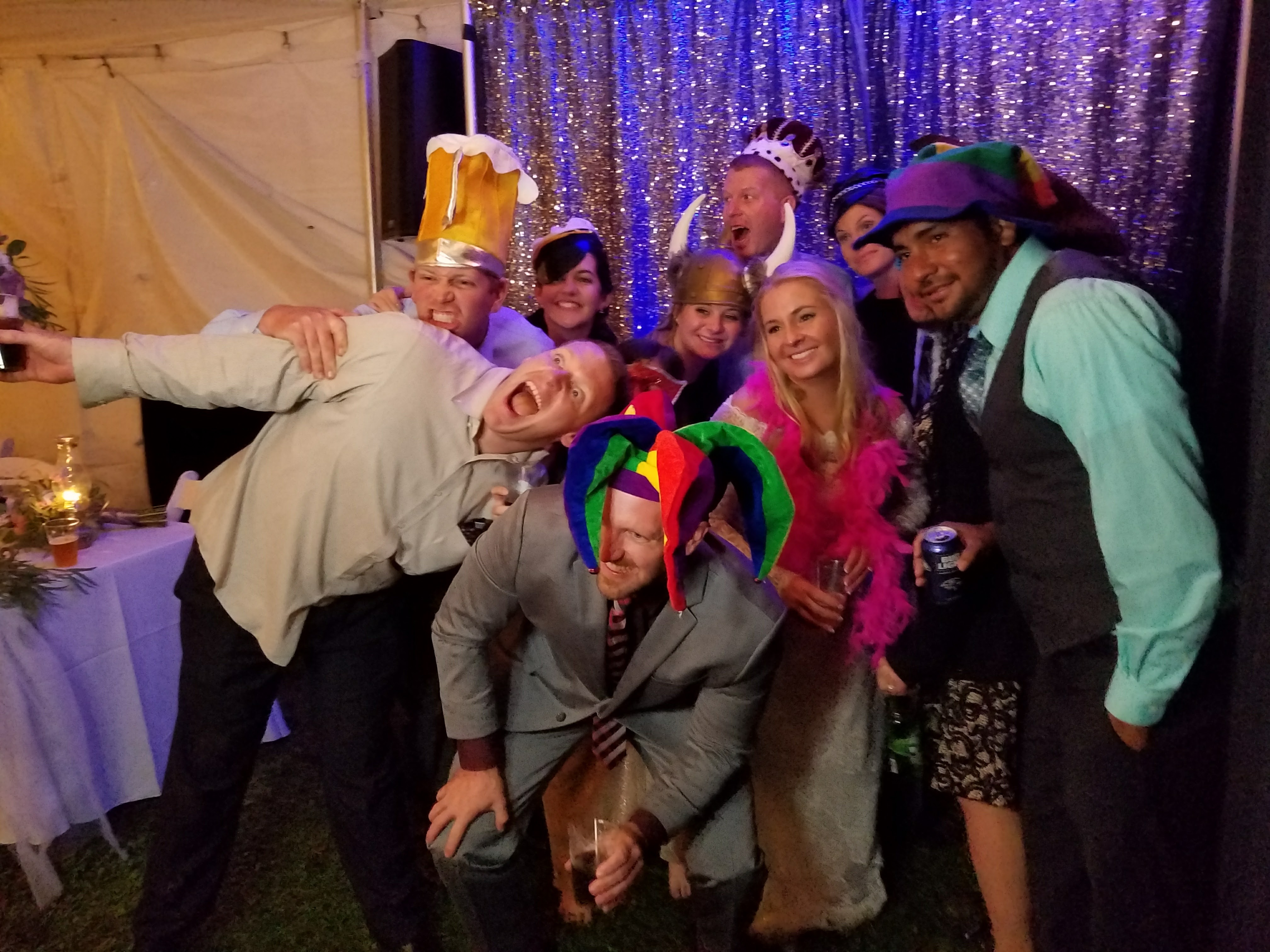 Wedding guests in jester hats and a viking helmet packed into one photo booth shot under the tent