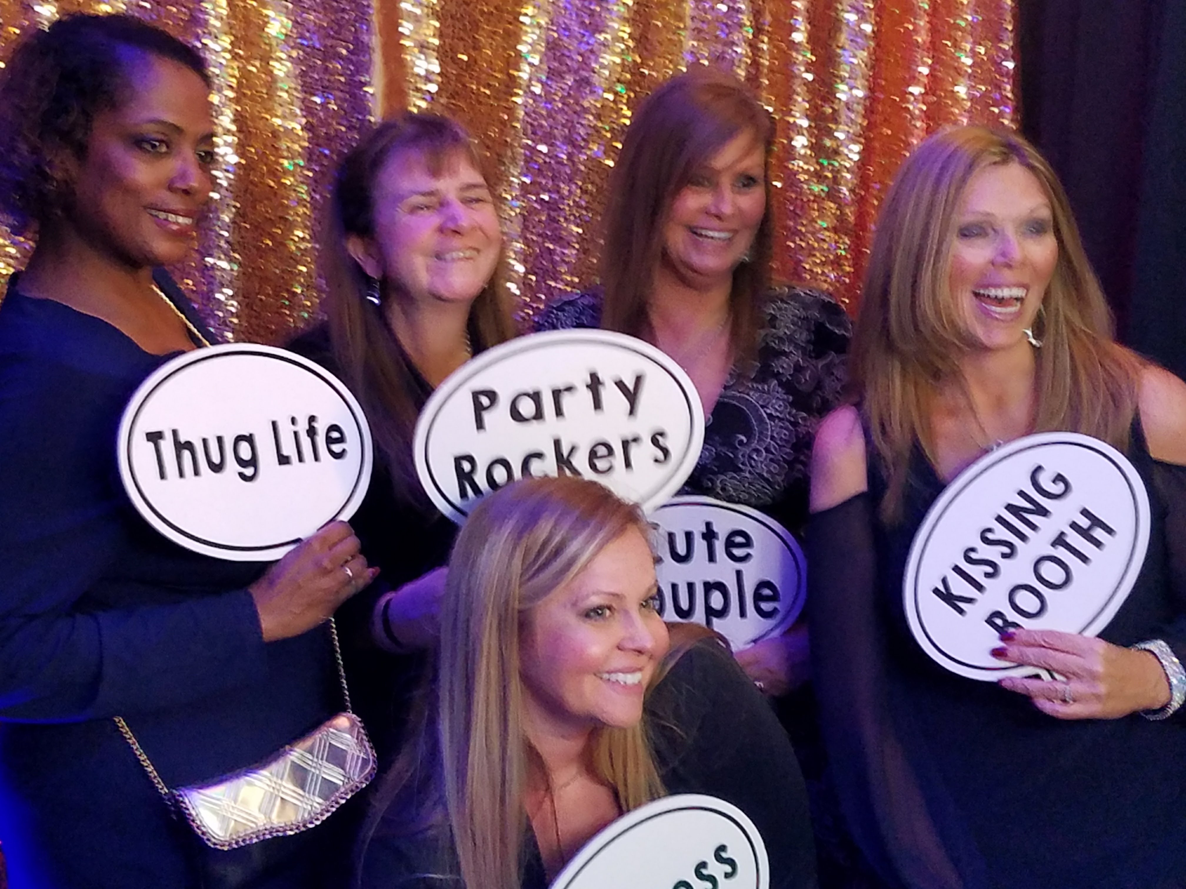Four guests holding “Thug Life” and “Party Rockers” prop signs in front of a gold sequin backdrop