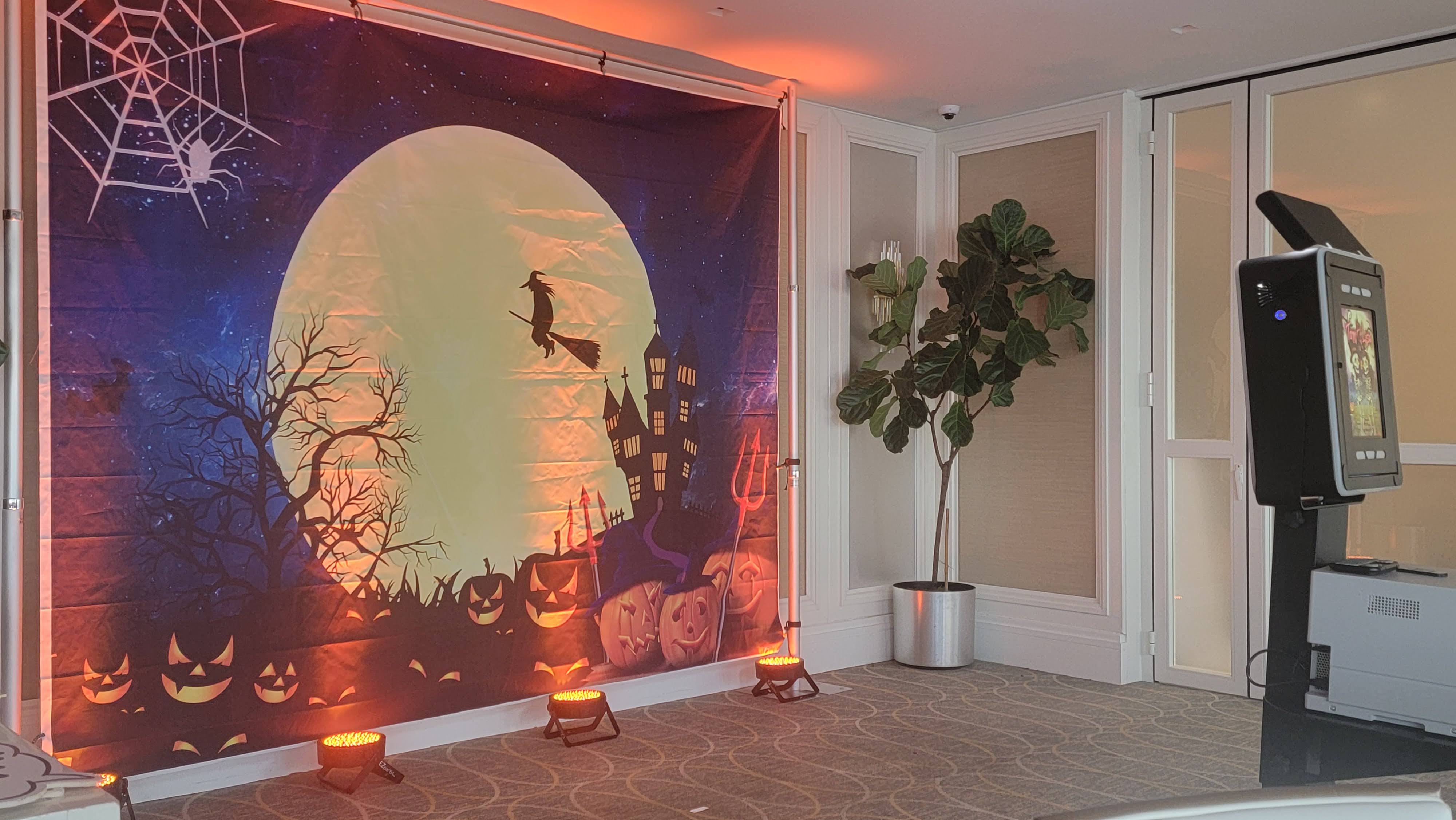 A Halloween photo booth backdrop of pumpkins and a witch, uplit beside the booth