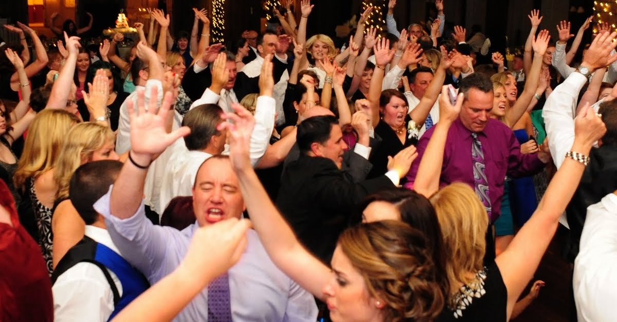 Close-up of a crowded reception dance floor, guests cheering with their hands in the air
