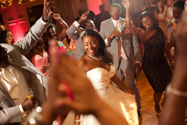 Smiling bride dancing in a warm-lit ballroom while family and friends dance around her