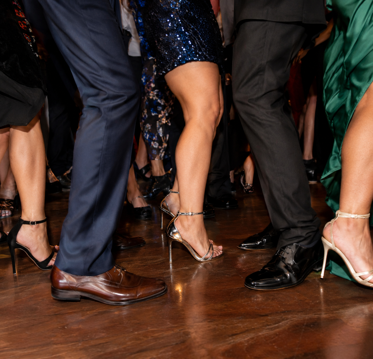 Close-up of wedding guests' feet in dress shoes and heels packed together on a hardwood dance floor